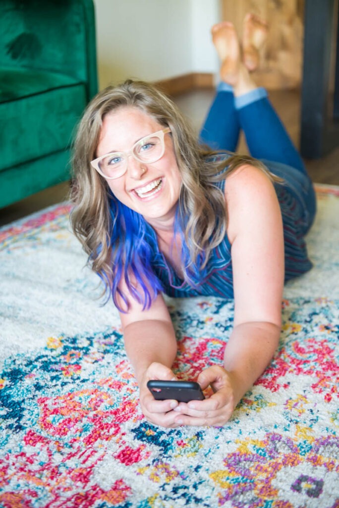 lindsey lockett laying on a colorful rug holding her phone and smiling